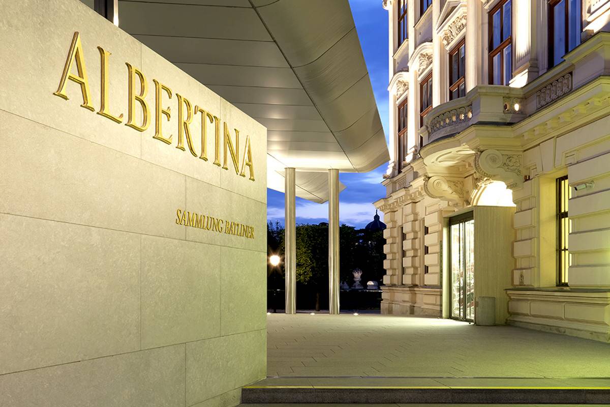 On the right, the entrance to the Albertina Museum with its historic façade. On the left on a wall the golden logo ‘ALBERTINA’ in elegant lettering | Credit: Photo © farbpraxis