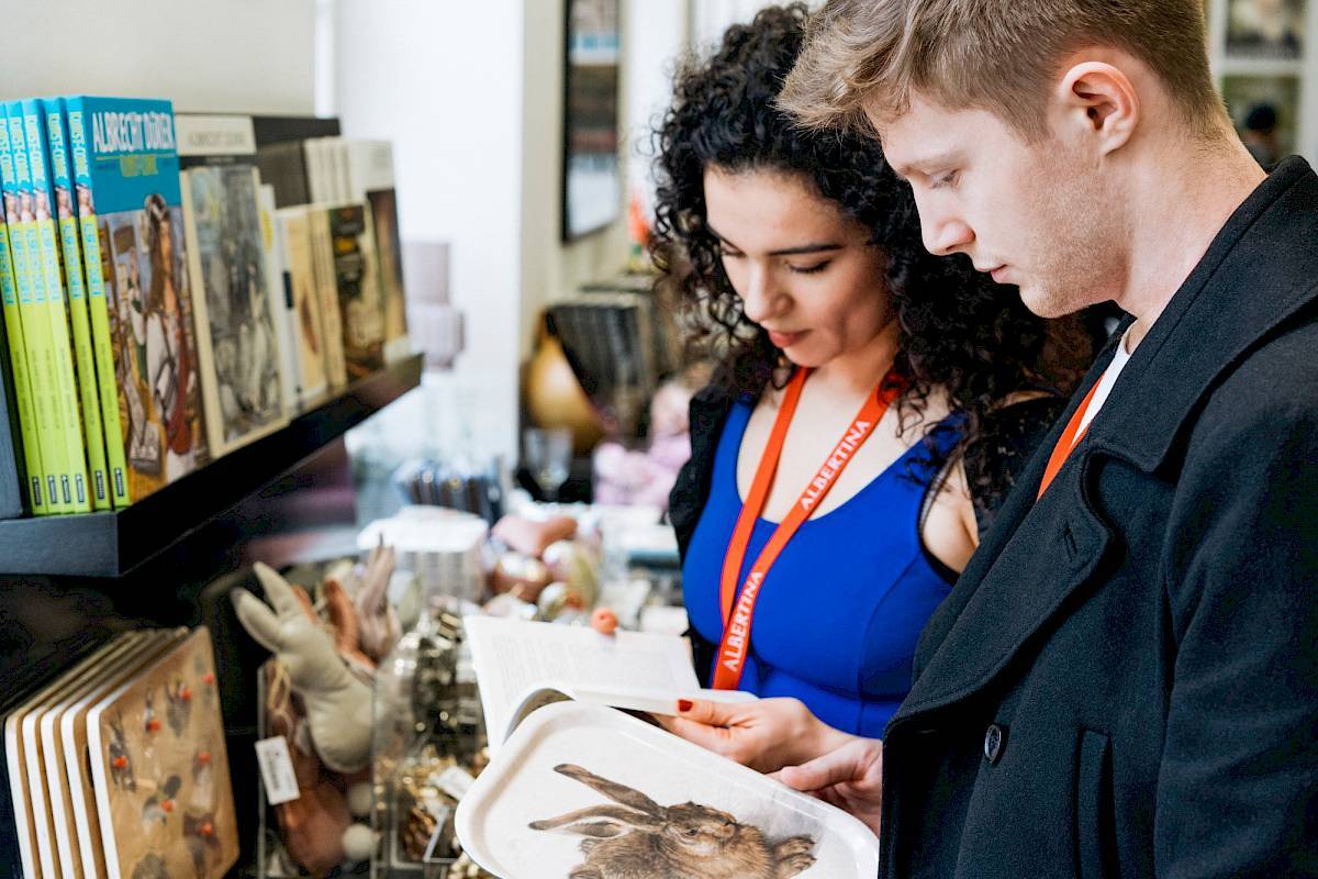 A woman looks at a book in the ALBERTINA store, next to her a man holds a tray with the Dürer hare motif | Photo © Marko Mestrovic