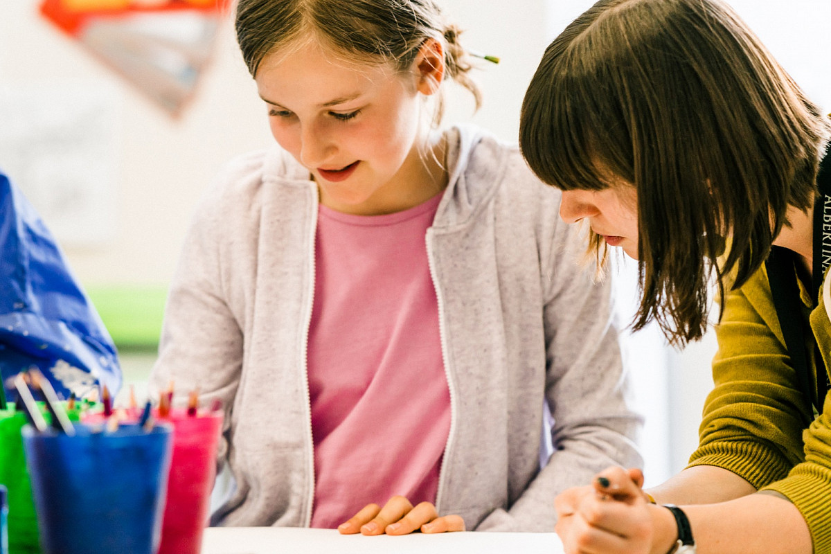 Child and woman working together at the table, in the foreground colored pencils in colorful cups. | Foto © Marko Mestrovic