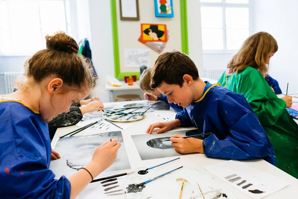 Several children in plastic aprons paint. In the middle a color palette with brushes | Photo © Marko Mestrovic