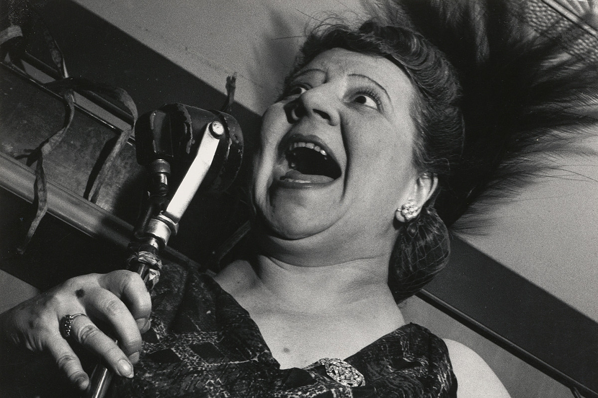 A woman in an evening dress holding a standing microphone up to her face. Her mouth is wide open. Credit: Lisette Model | Singer at the Cafe Metropole, New York City, 1946 | ALBERTINA Wien © 2025 Estate of Lisette Model, courtesy Lebon, Paris / Keitelman, Brussels