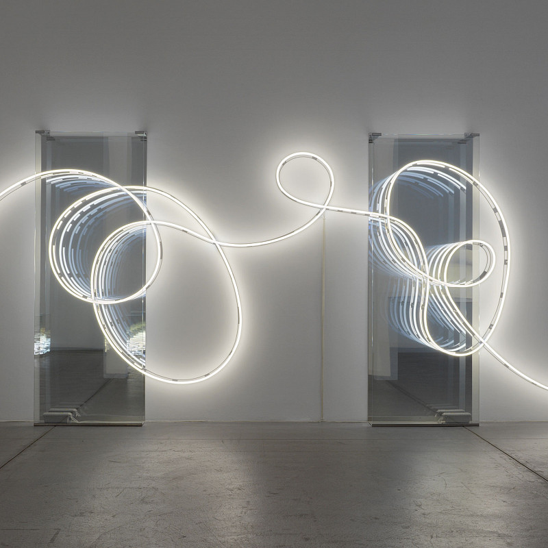 Blick in dunklen Ausstellungsraum, der nur von einer geschwungenen Lichtinstallation vor einem Spiegel beleuchtet wird. | Brigitte Kowanz | Email 02.08.1984 03.08.1984, 2021 | ESTATE BRIGITTE KOWANZ © Estate Brigitte Kowanz / Bildrecht, Wien 2025 | Foto: Peter Hoiss