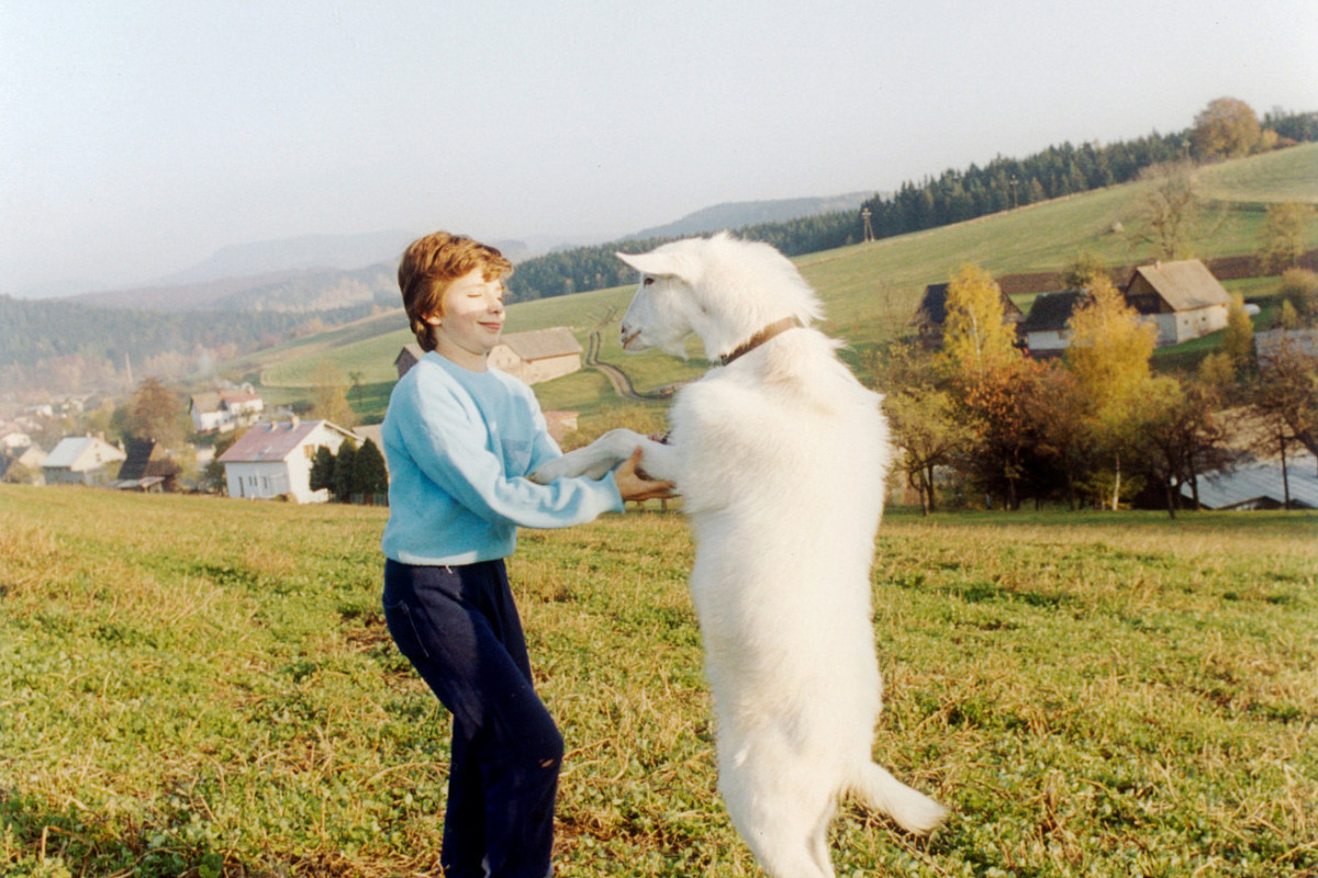 A woman is standing in a field. Opposite her, a white goat is standing upright. The woman is holding the animal's front legs with her hands. Credit:Jitka Hanzlová | Untitled, 1993 / from the series: Rokytník, 1990 – 1994 | Courtesy of the artist © Jitka Hanzlová / Bildrecht, Vienna 2025