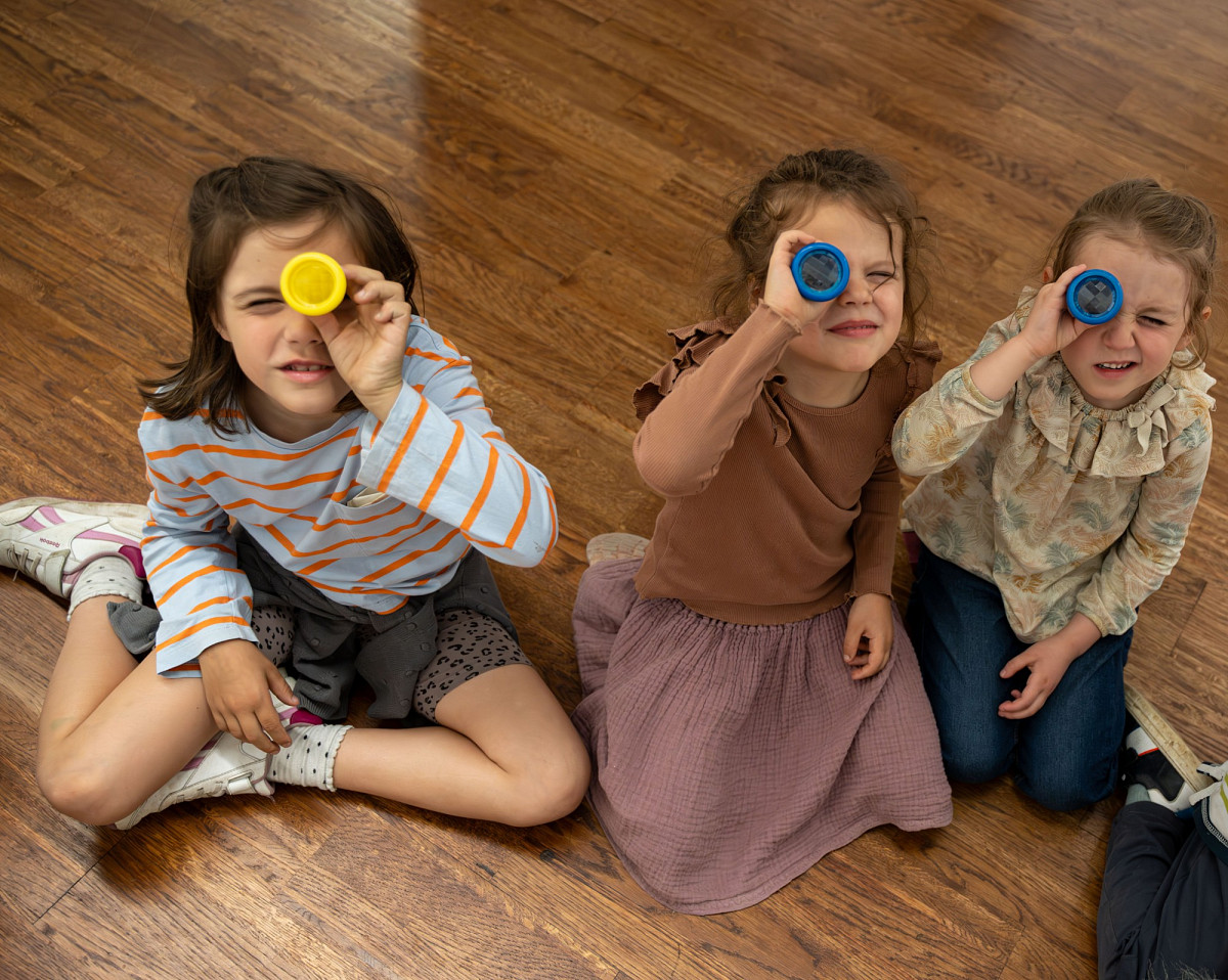 Three children sit on the floor and look towards the camera. | Photo © Daniel Antalfi