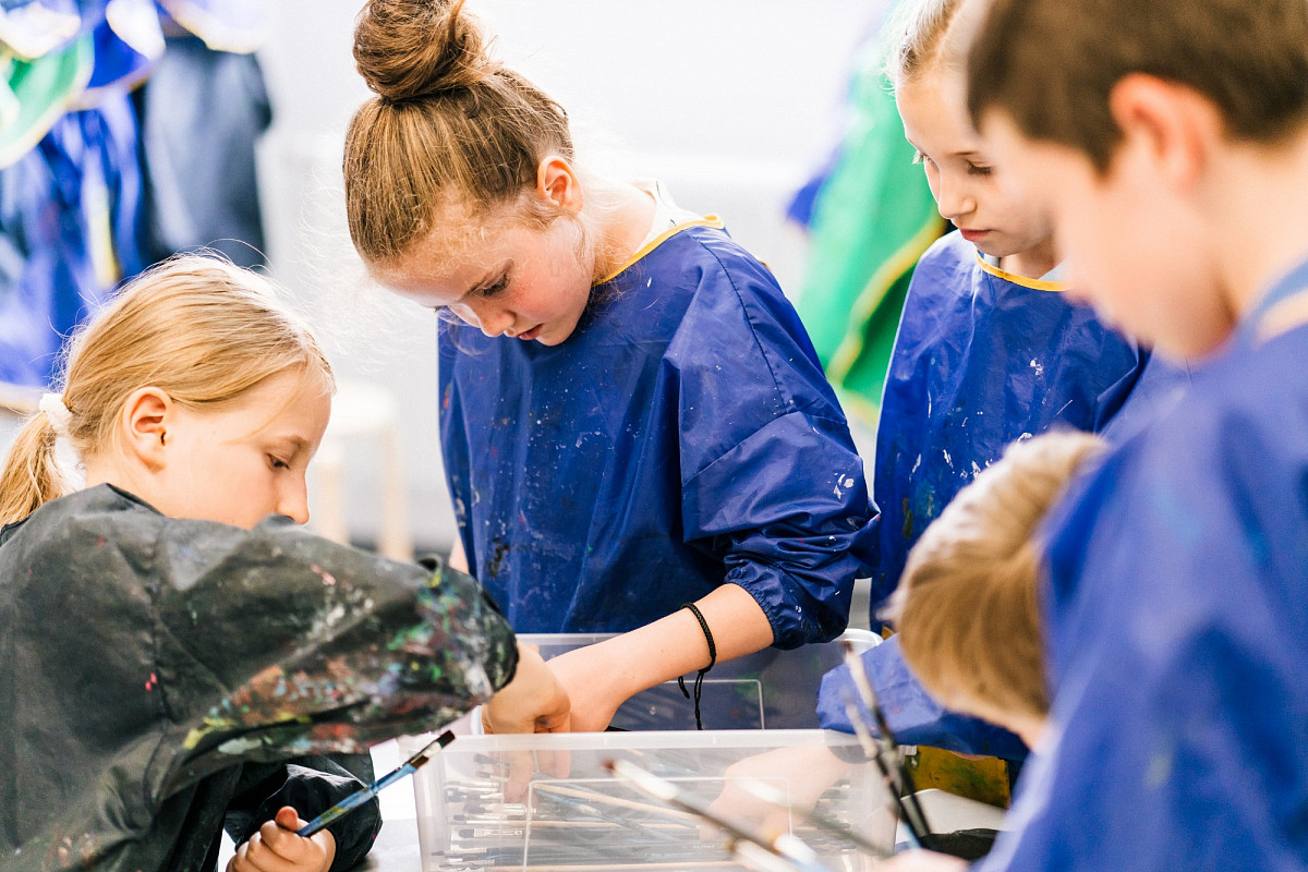 Children in paint coats stand around a box full of brushes and pick up | Foto © Marko Mestrovic