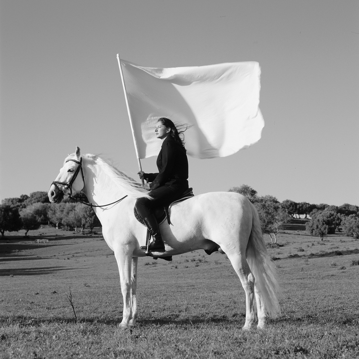 Black and white photograph of the artist sitting on a white horse and holding a large white flag.