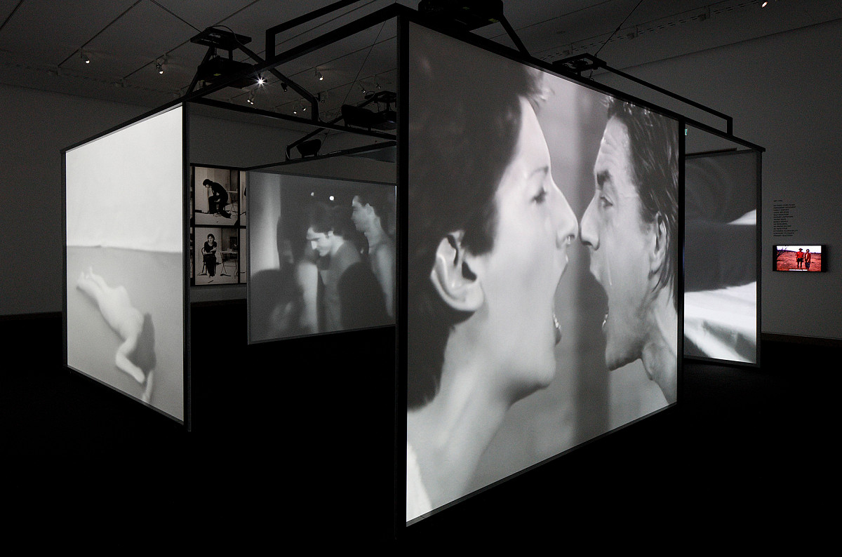 View of the exhibition installation: Several video screens hung side by side, forming a separate room. The screens show black-and-white videos depicting the artist's actions.