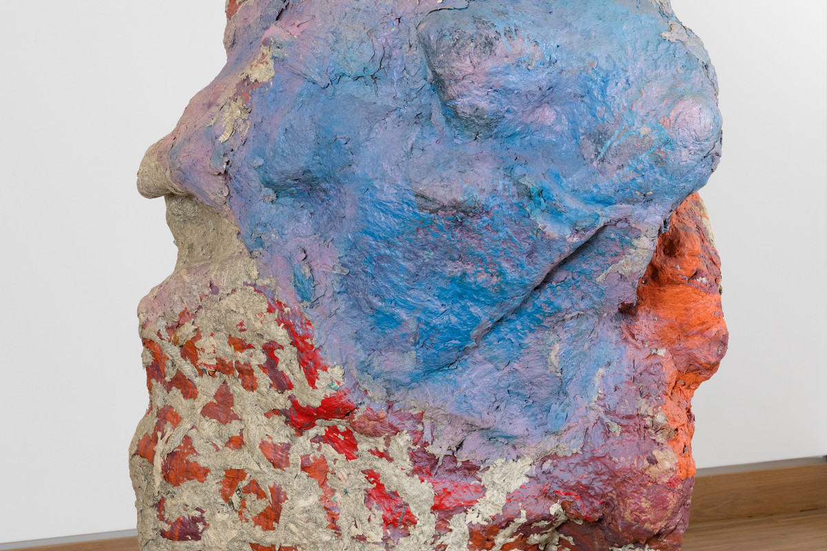 Sculpture in the form of a large stone standing on wooden boards and painted in shades of red and blue.