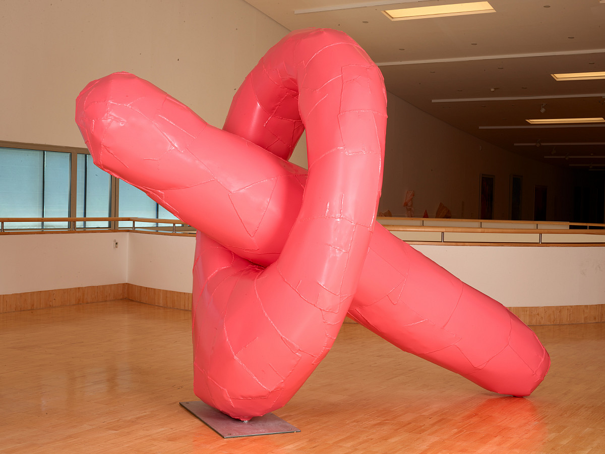 Large pink sculpture with an elongated object passing diagonally through the hole in the middle of an upright circle.