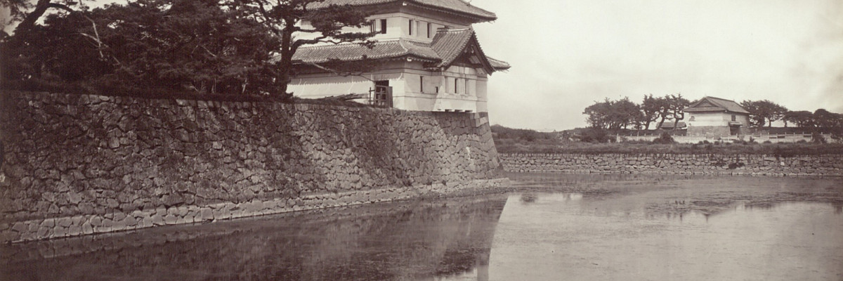 Black-and-white photograph of a Japanese-style guardhouse on the edge of the moat, surrounded by trees.