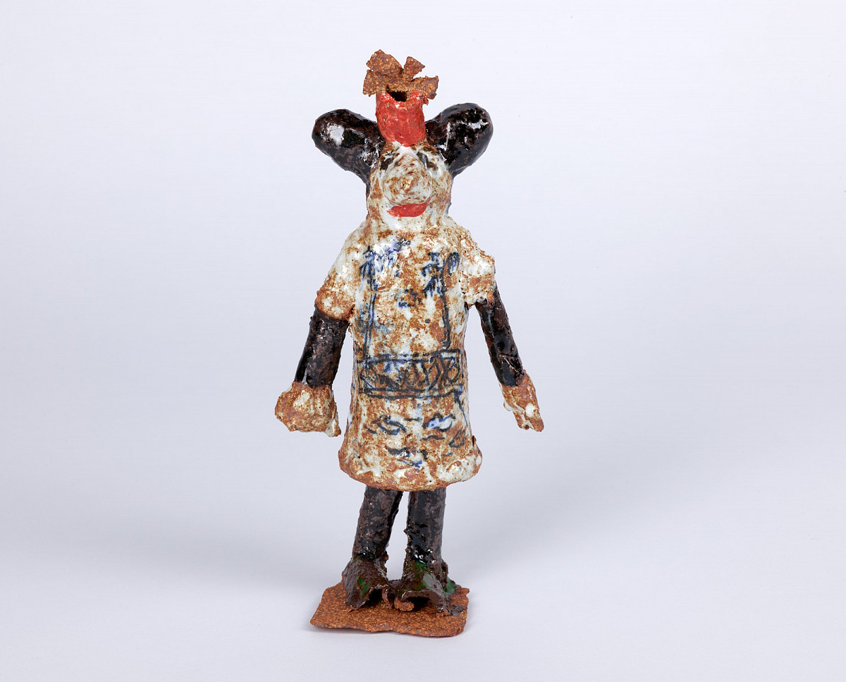 Sculpture of a mouse-like, standing figure with a red hat and blue patterned robe.