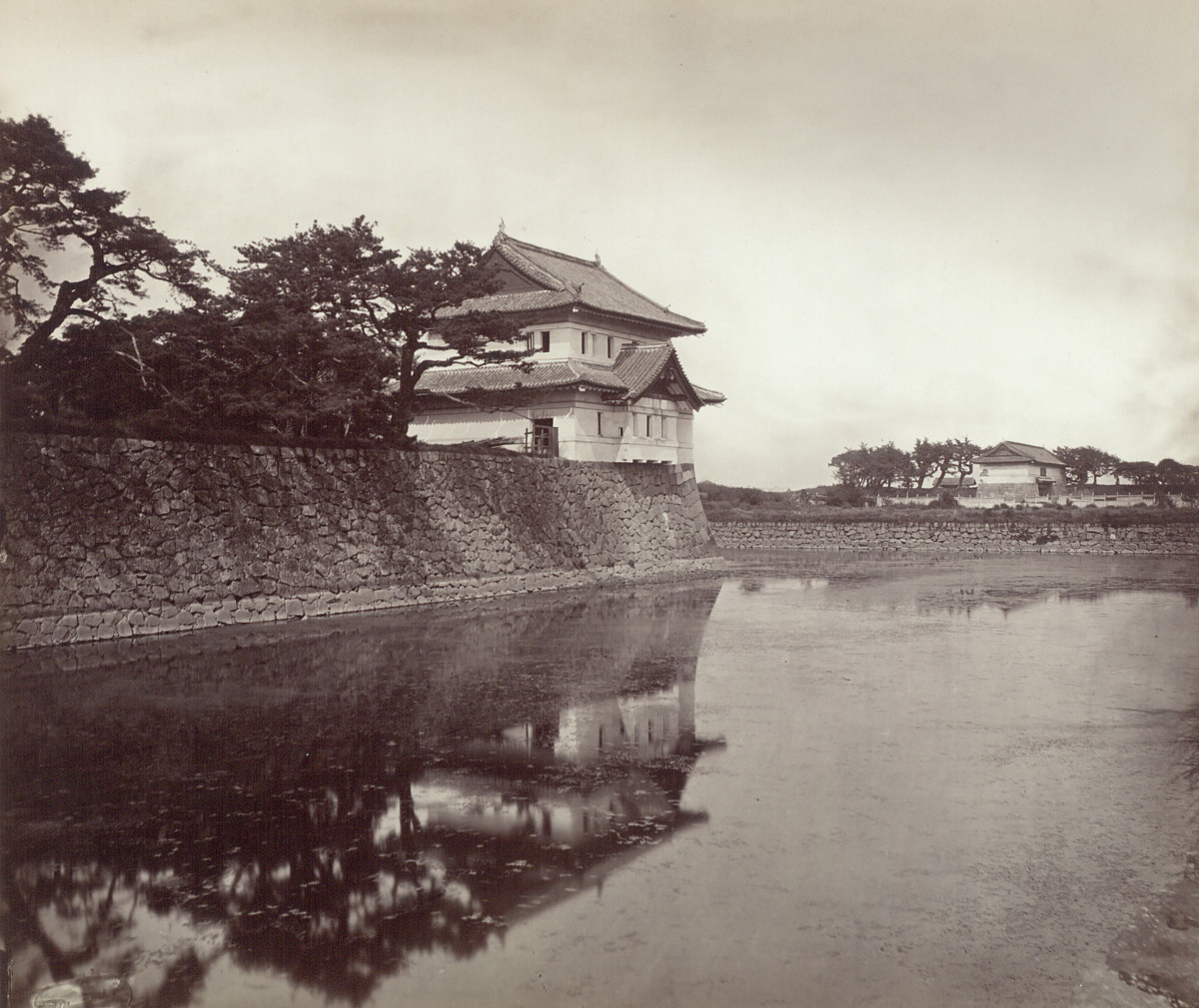 Black-and-white photograph of a Japanese-style guardhouse on the edge of the moat, surrounded by trees.