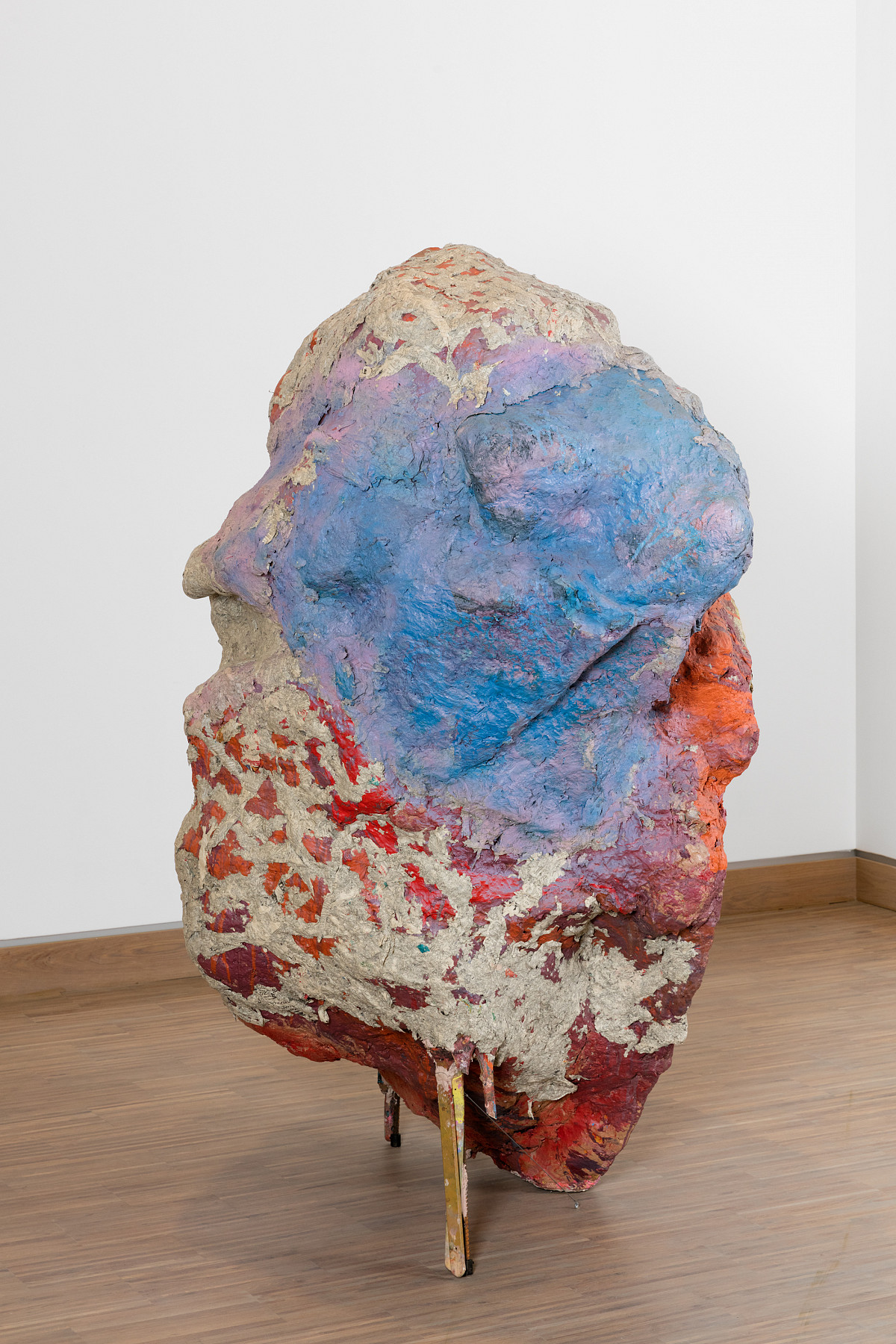 Sculpture in the form of a large stone standing on wooden boards and painted in shades of red and blue.
