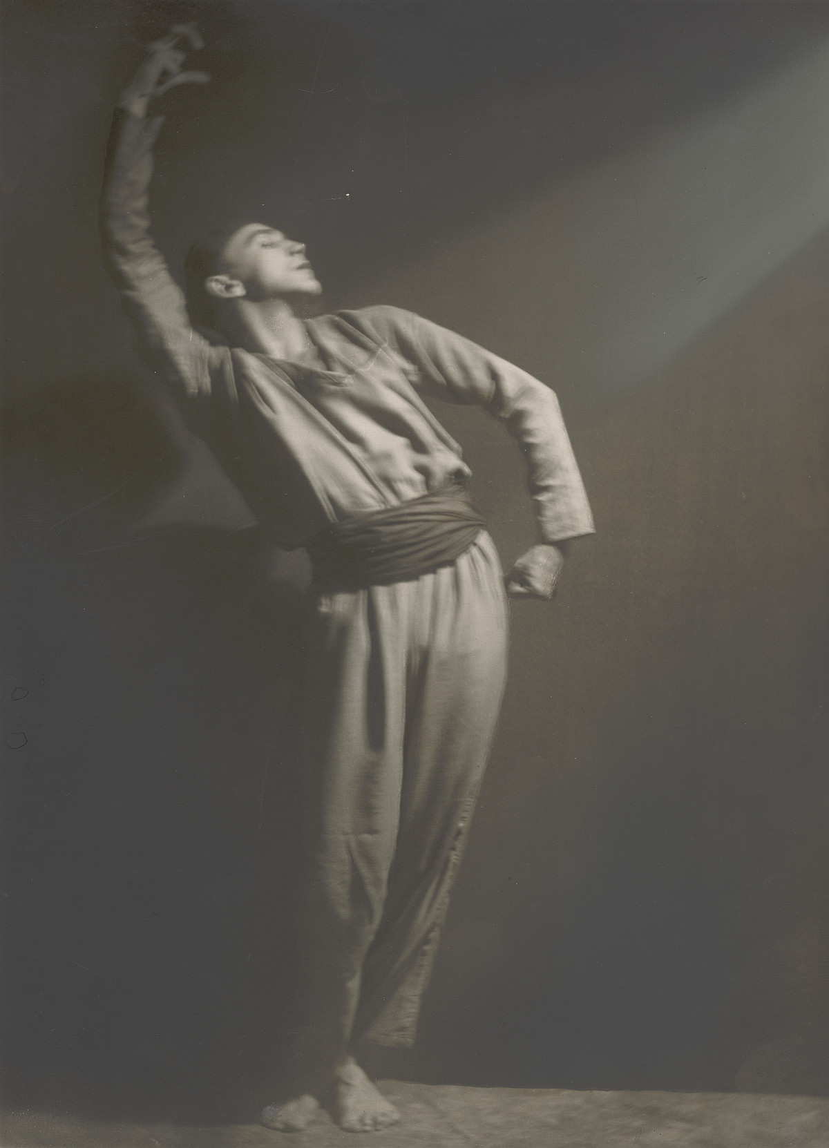 Ein Mann in einem langärmeligen Tanzkostüm, der Körper ist gebogen, ein Arm nach oben gestreckt, der andere zeigt nach unten.