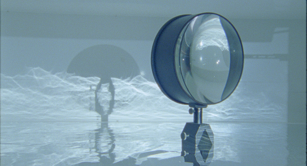 A large magnifying glass that casts a shadow onto a water-like projection on the wall.