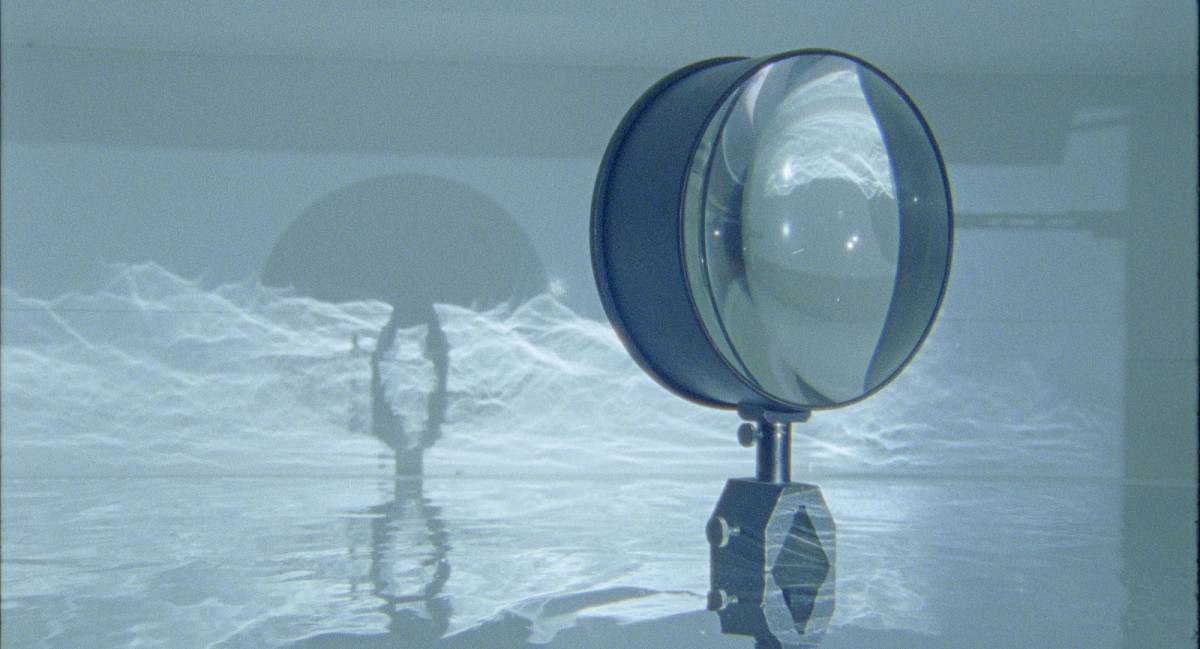 A large magnifying glass that casts a shadow onto a water-like projection on the wall.
