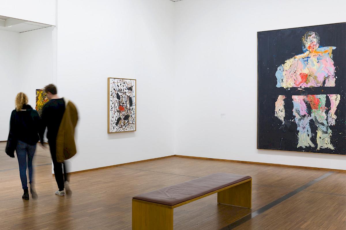 Two people walk through an exhibition hall, pictures to the left and right, a bench in the middle | Photo © Mario Kiesenhofer