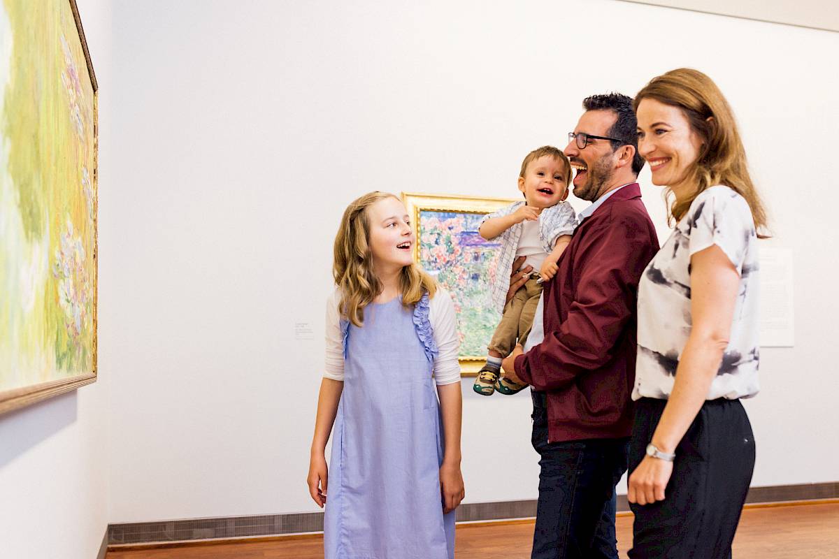 A family with a young girl and a toddler in the Monet to Picasso exhibition, with Monet's famous water lily pond in front of them. | Photo © Marko Mestrovic